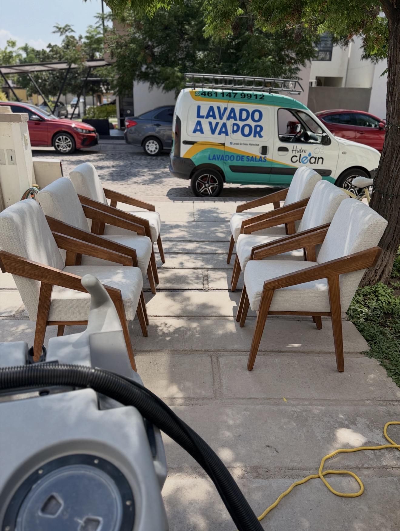 Conjunto de sillas blancas de madera en exterior con camioneta de Hidroclean al fondo.